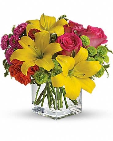 Bouquet of yellow lilies, pink roses, and green button mums in a clear square vase