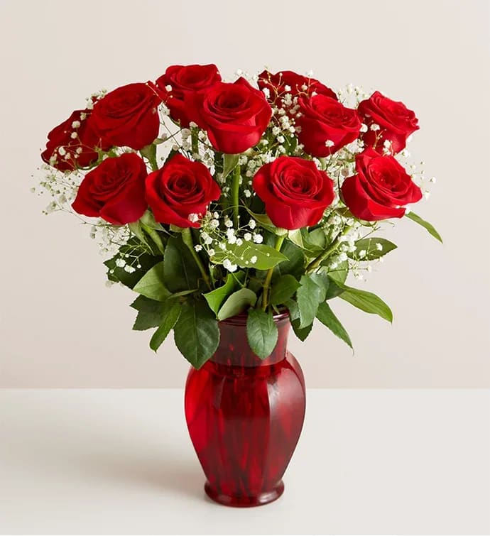 Red roses arranged in a red glass vase with baby's breath