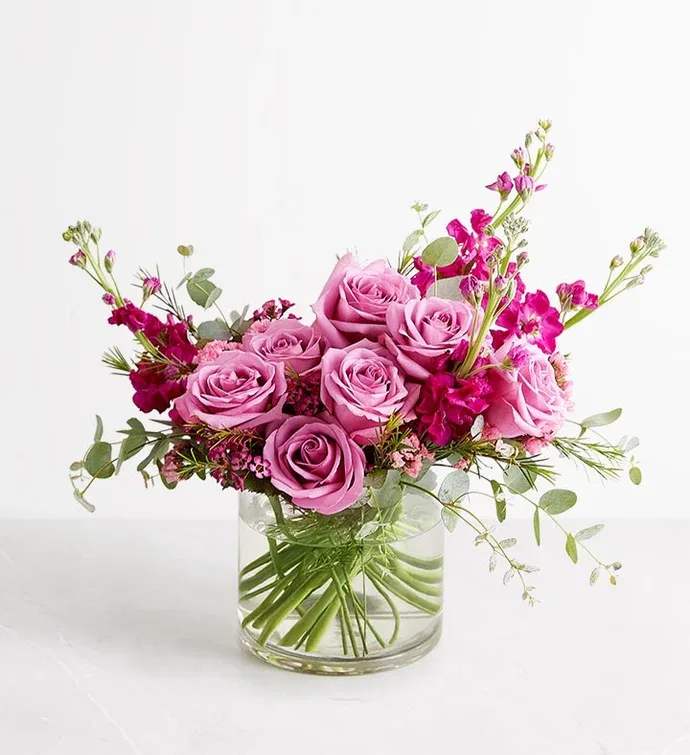 Pink roses and magenta flowers arranged in a clear glass vase