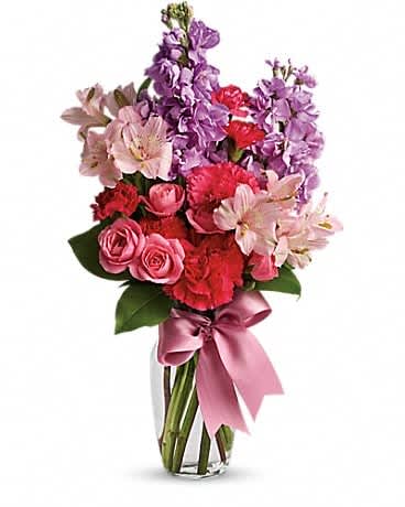 Bouquet of pink, red, and purple flowers in a glass vase with a pink ribbon