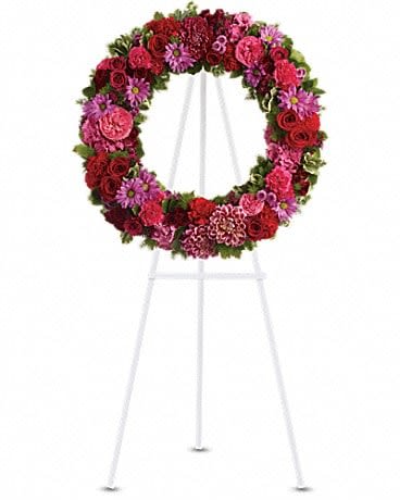 Circular floral wreath on a white easel with red and pink blooms