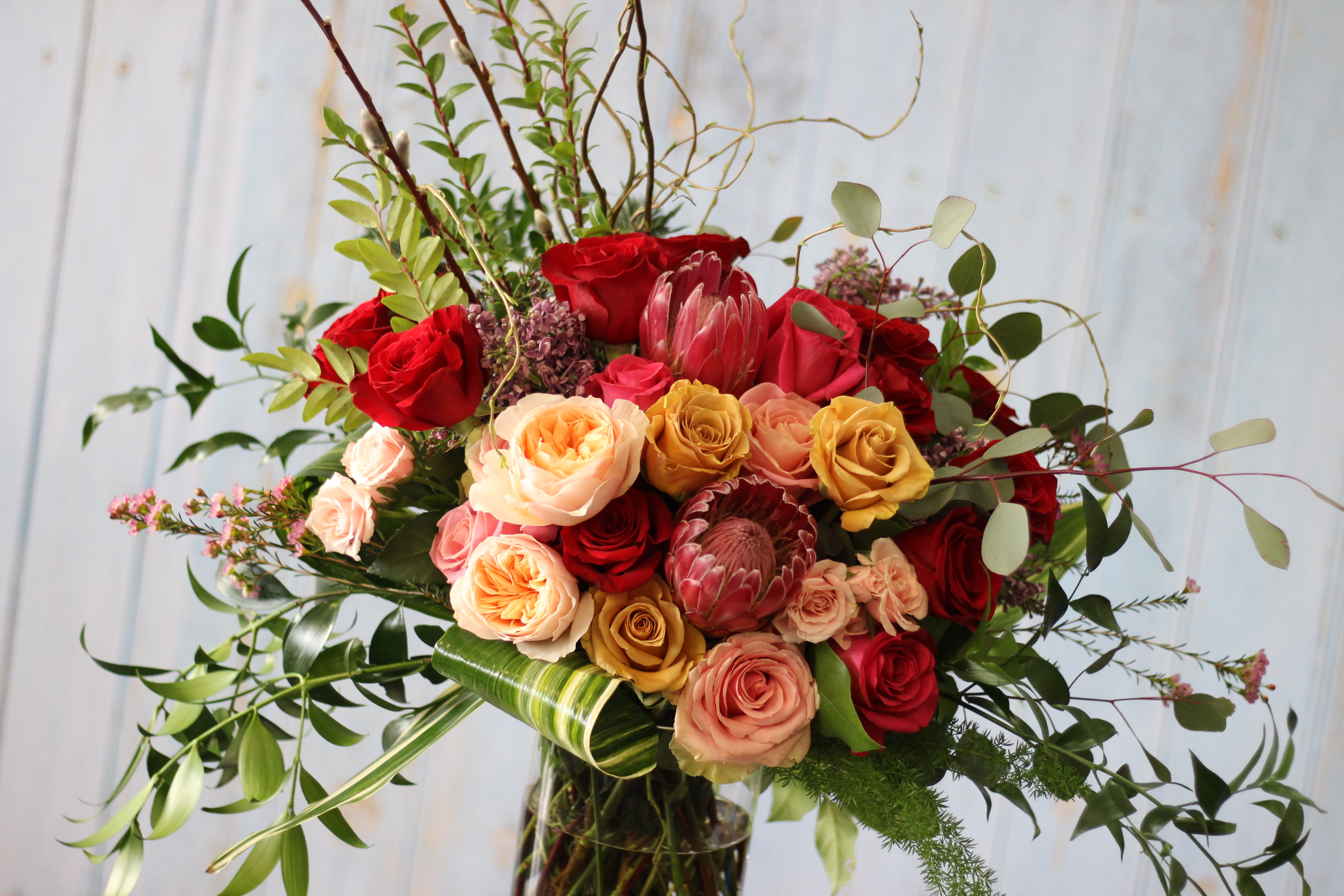 Mixed bouquet of red, peach, and yellow roses with greenery in a glass vase