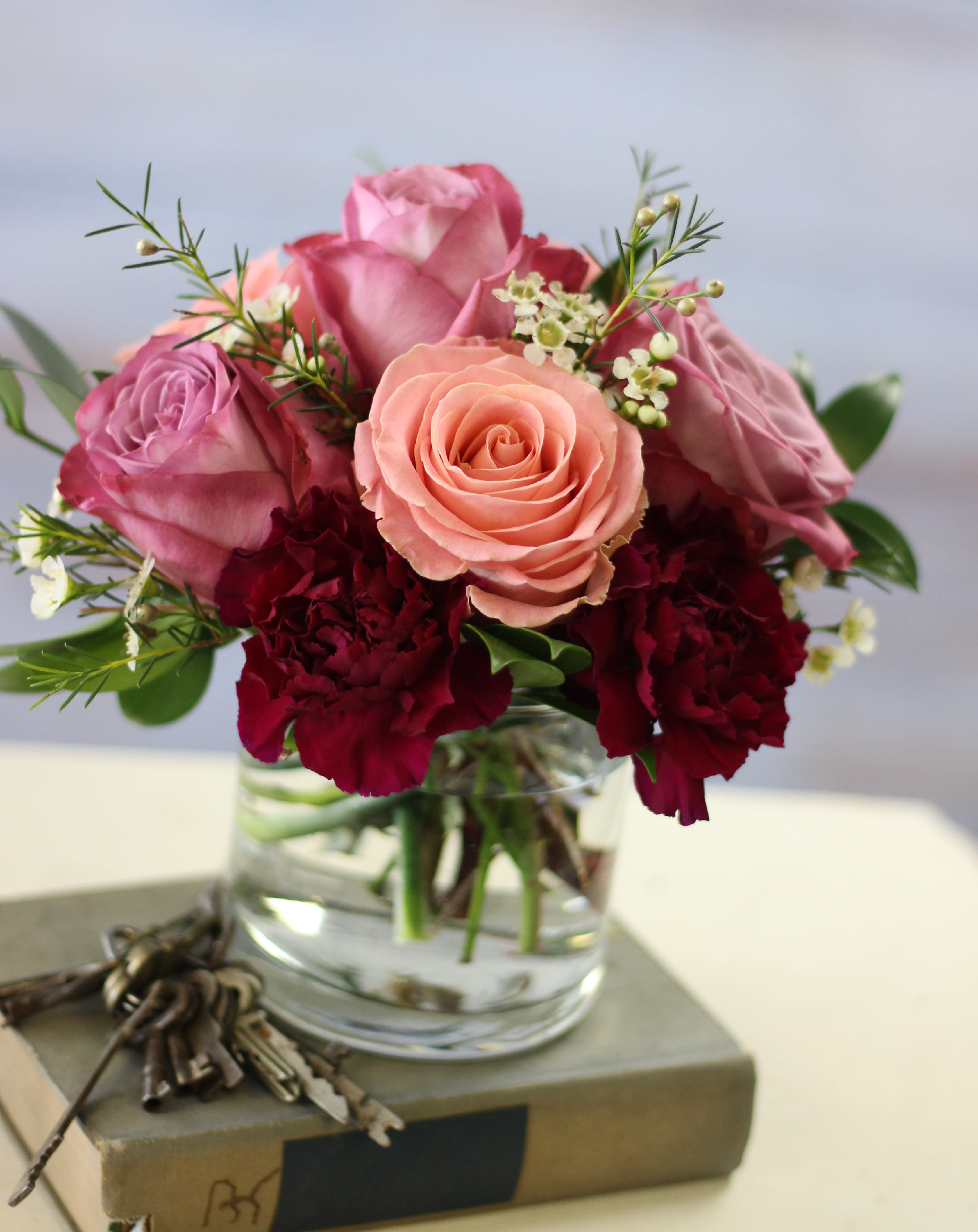 Pink and peach roses with burgundy carnations in a glass vase
