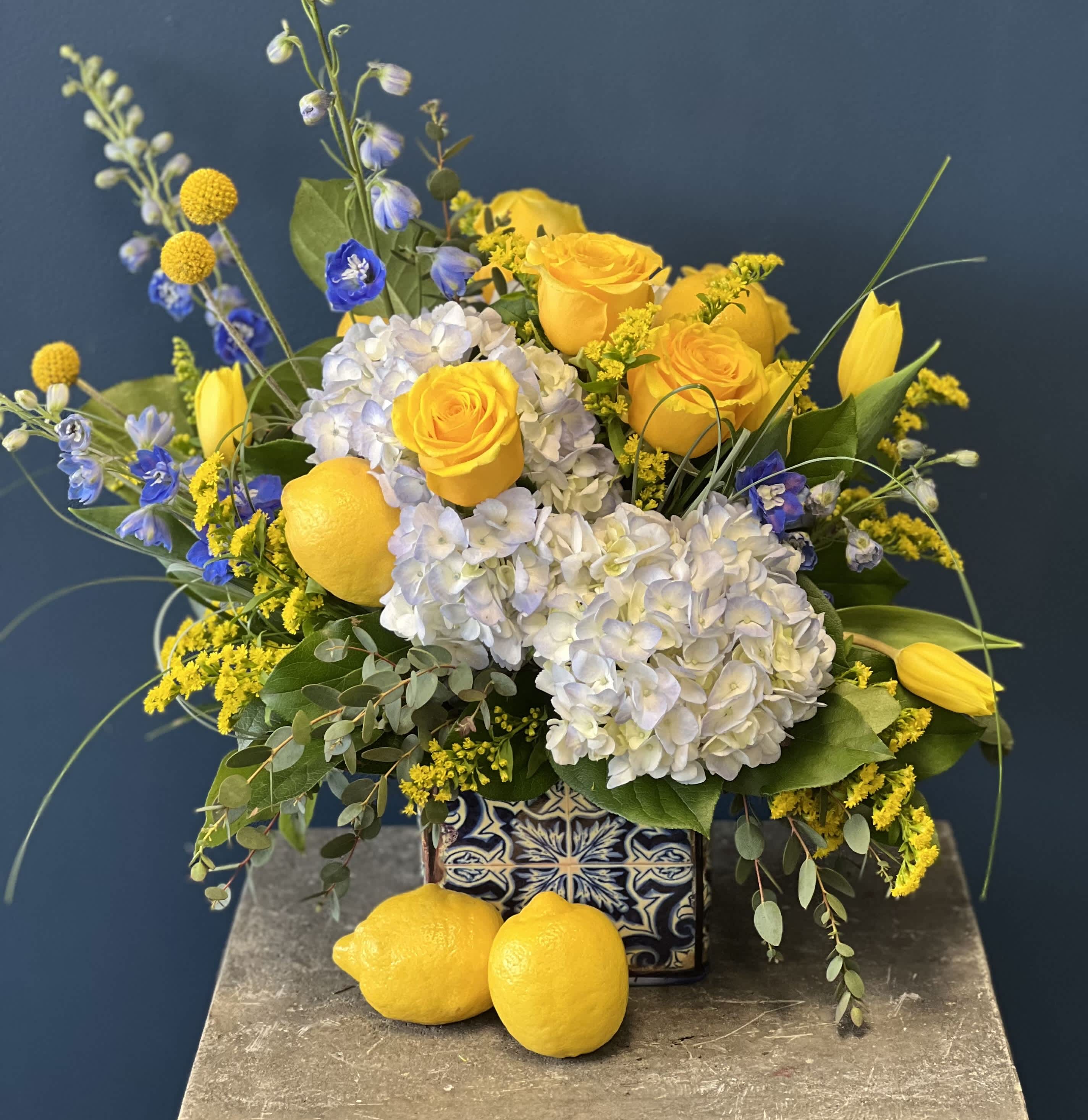 Yellow roses and white hydrangeas in a patterned ceramic vase with lemons