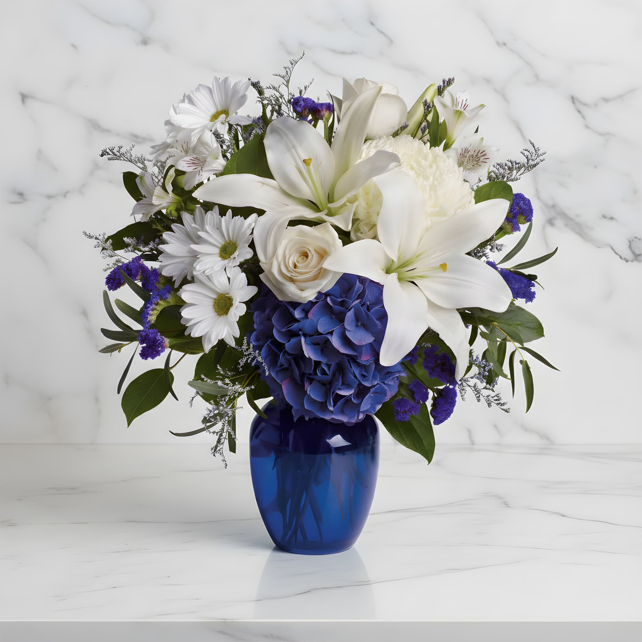 White lilies, daisies, and blue hydrangea in a cobalt vase