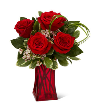 Red roses arranged in a red glass vase with green foliage