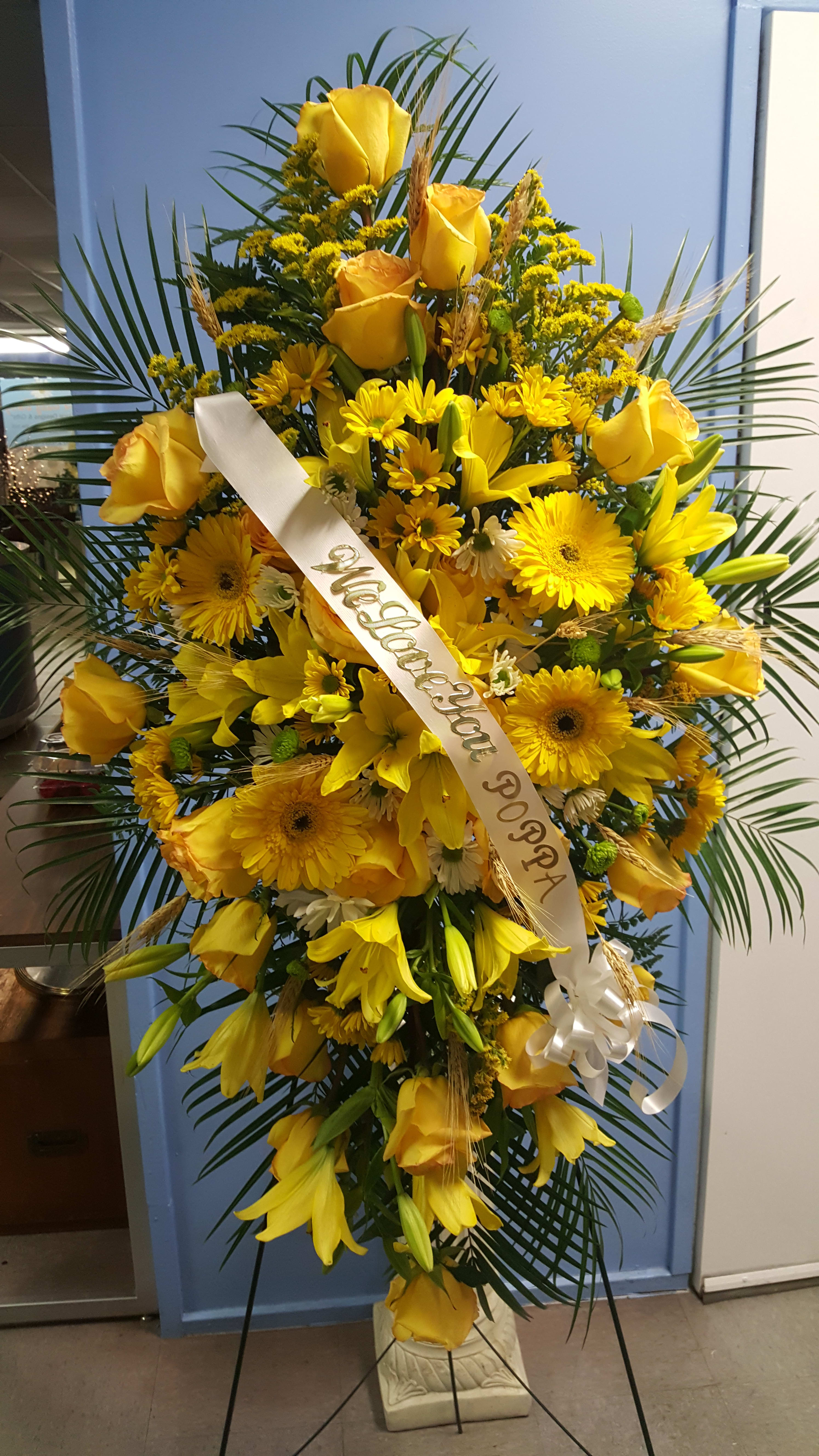 Tall yellow floral standing spray with a white ribbon on an easel