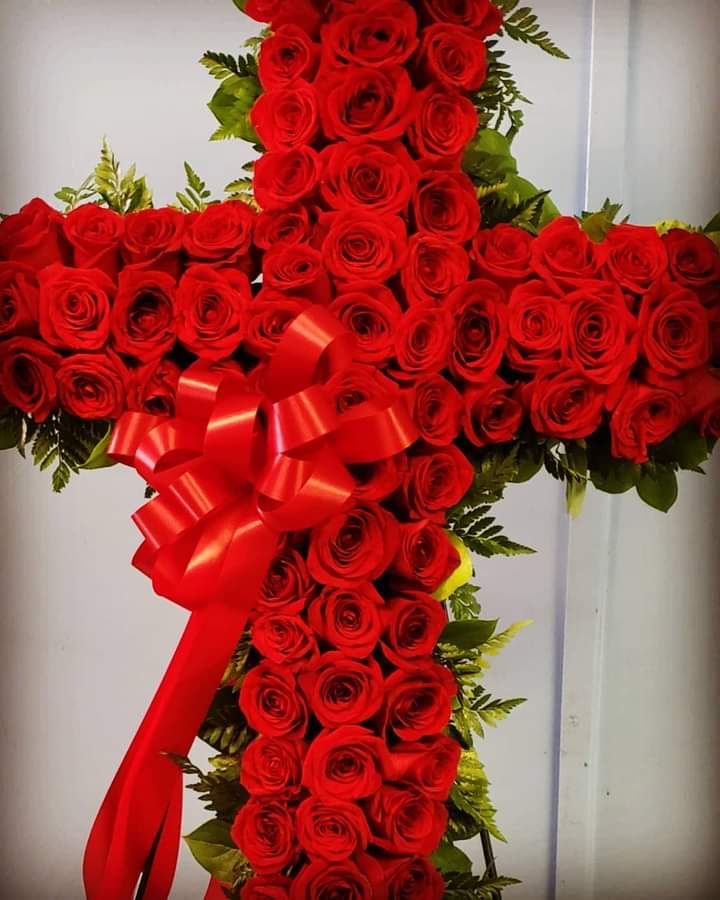 Cross-shaped arrangement of red roses with a red ribbon bow
