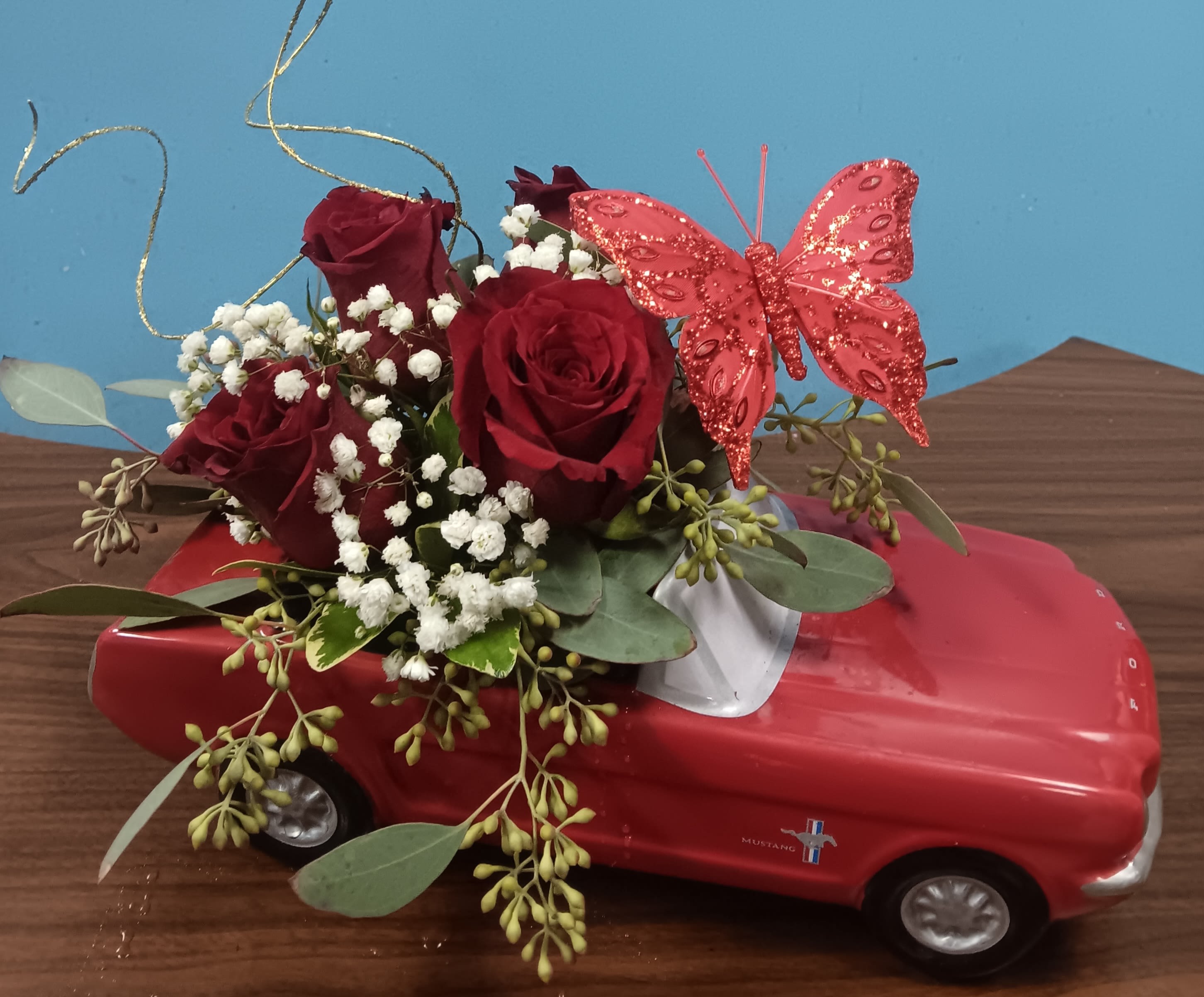 Red roses and baby's breath arranged on a red toy car with a pink butterfly