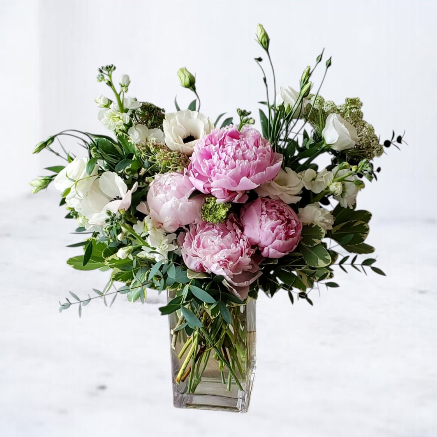 Harmony - Soft, romantic, and effortlessly elegant, Harmony Bouquet is a delicate fusion of grace and charm.  Lush pink peonies take center stage, their ruffled petals symbolizing love and prosperity. Pure white stock adds a touch of fragrance and airy elegance, creating a beautiful contrast. The striking anemones, with their dark centers, introduce a touch of drama and sophistication, while lisianthus enhances the bouquet with its delicate, flowing petals and timeless beauty. Our Substitution Guidelines: Same or Higher Value: Any substituted flower will be of equal or greater value, ensuring your arrangement maintains its beauty and quality.  Similar Color Palette: We will replace flowers with alternatives that closely match the original color scheme and overall aesthetic of the arrangement.  Maintaining Design Integrity: The overall style, shape, and theme of the bouquet will be preserved, ensuring a look as close as possible to the original design.