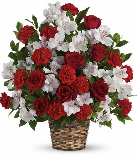 Red roses, red carnations, and white alstroemeria arranged in a woven basket