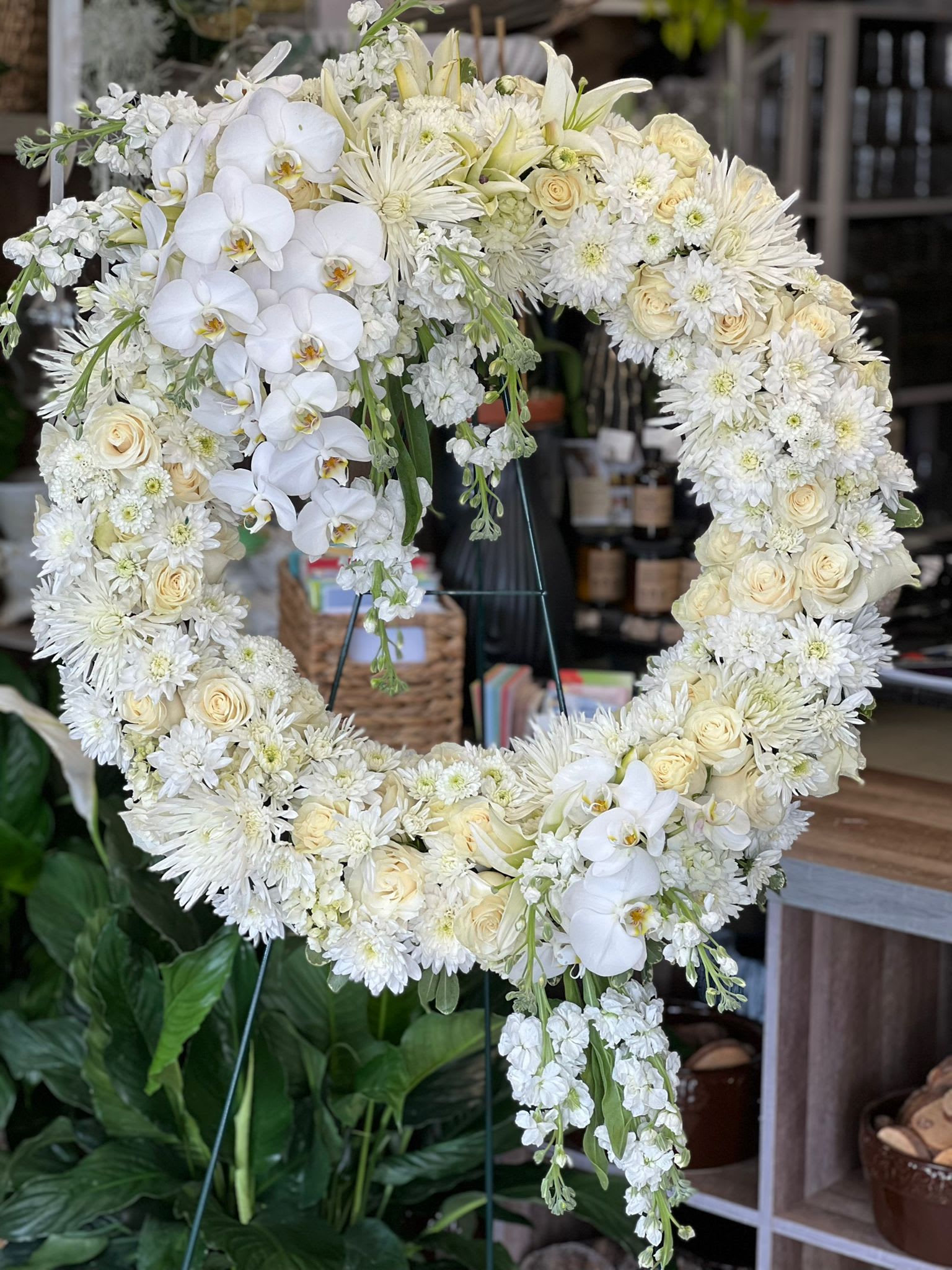 Large white and cream floral wreath with roses, orchids, and mums on a stand