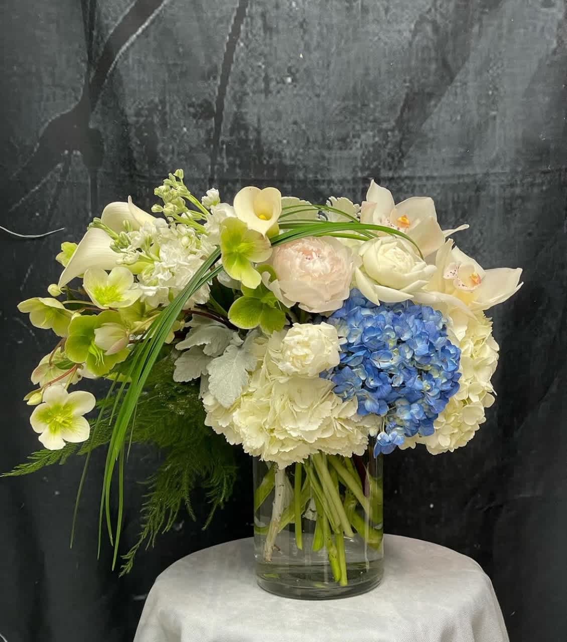 Sky High - An elegant arrangement in shades of white and soft blue. Featuring Hellebores, White and Blue Hydrangeas, White Peonies, White Stock, White Calla Lilies, White Cymbidiums, Dusty Miller, and Lily Grass — this design evokes lightness and luxury.  ***Note: When peonies are out of season, they may be substituted with similar blooms of equal value.  Please Note: To ensure the best availability and freshness, this arrangement requires TWO DAYS advance notice. Not available for same-day delivery or pickup. Feel free to contact our store with any questions. Thank you for your understanding.