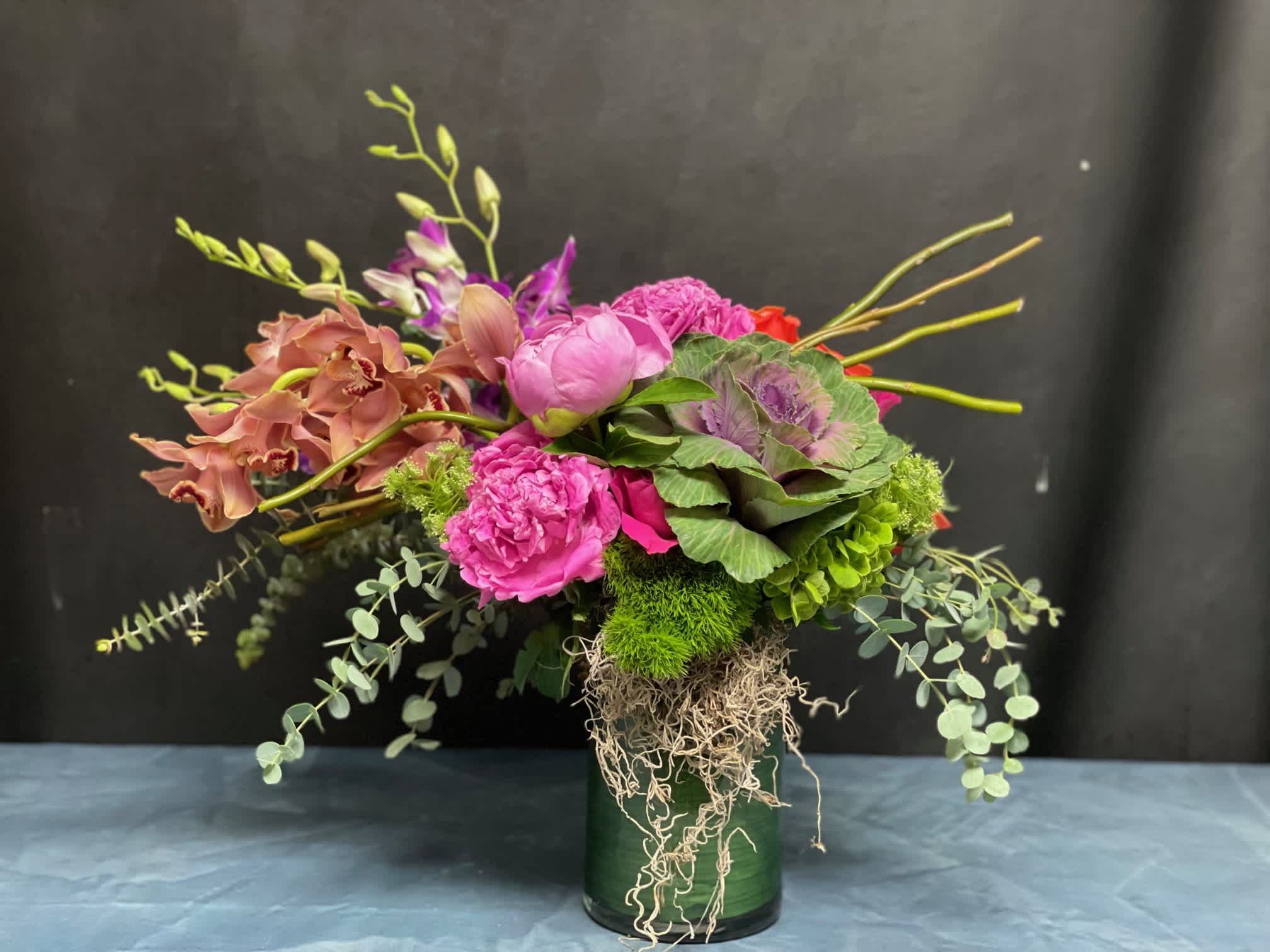 Asymmetrical arrangement with pink peonies, peach orchids, and green accents in a glass cylinder vase