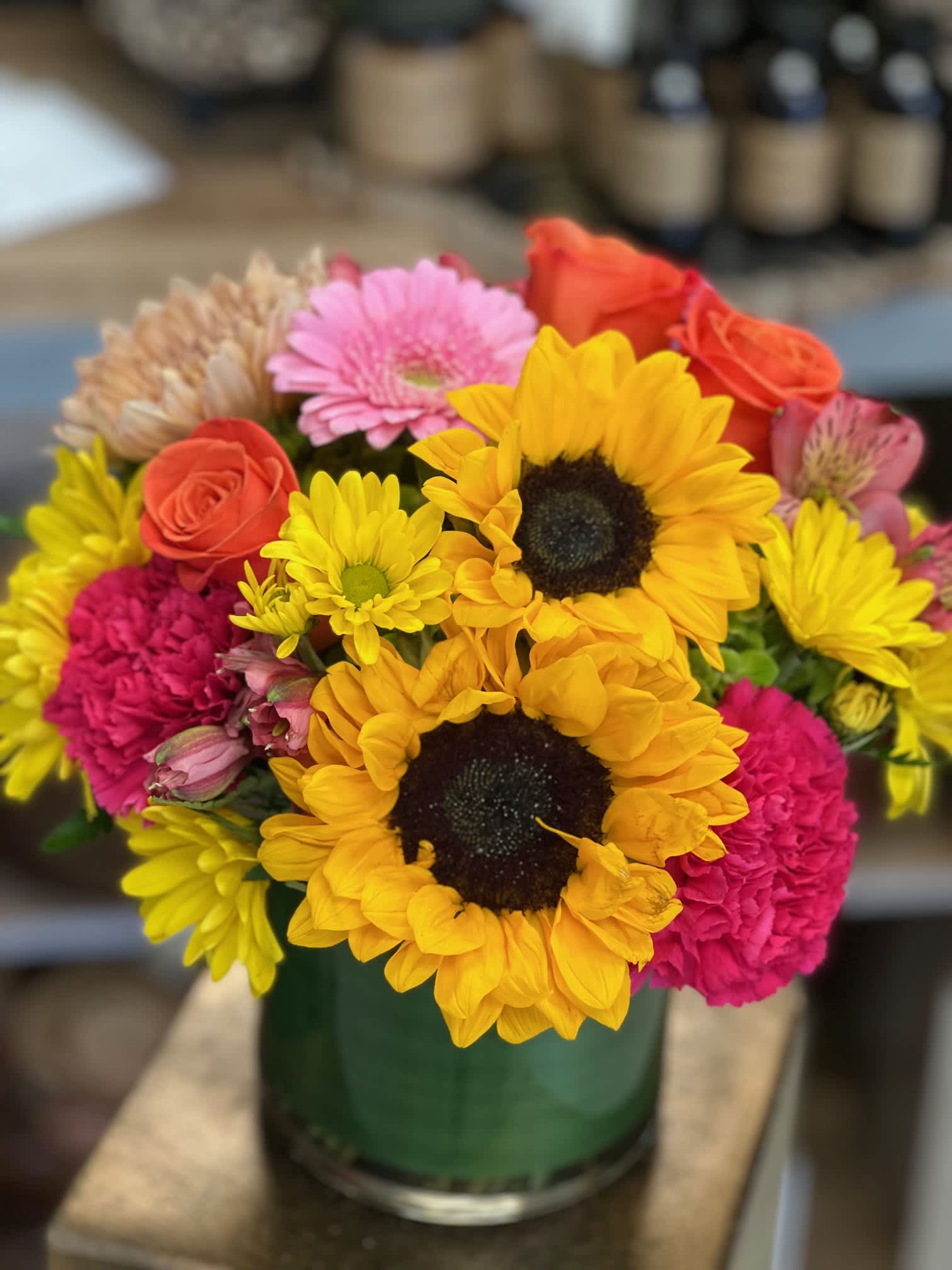 Bright mixed bouquet with sunflowers, roses, gerbera and carnations in a green glass vase