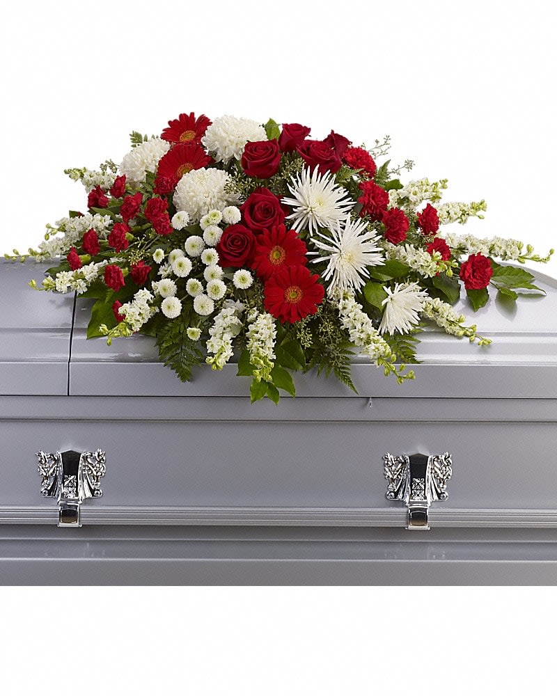 Strength and Wisdom Casket Spray - This beautiful red and white spray will deliver strength and the wisdom to know that there will be brighter days ahead. Dazzling red roses and gerberas, brilliant white chrysanthemums and larkspur are arranged with gentle greens to create a strong yet soothing arrangement.Approximately 39" W x 21" H