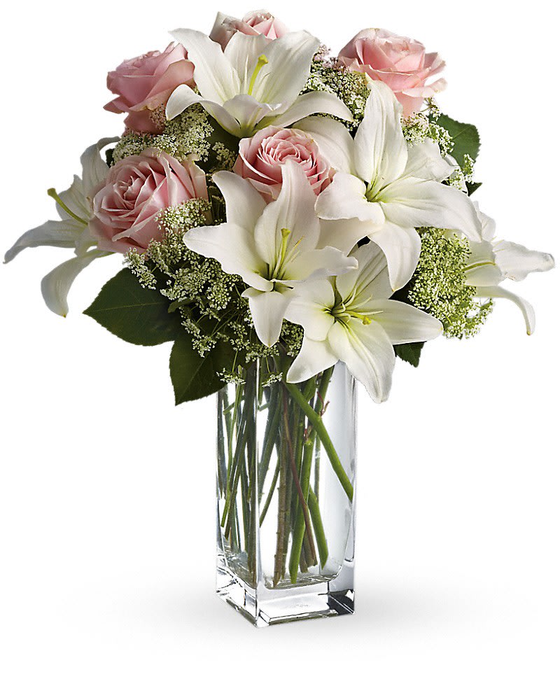 Tall glass vase arrangement of white lilies, pale pink roses, and small white filler flowers.