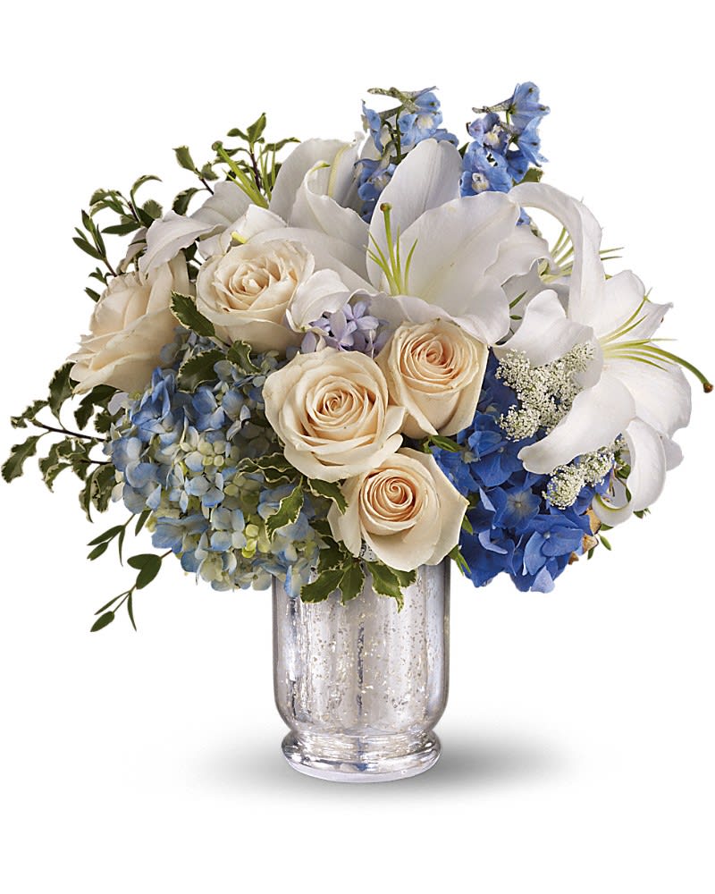 Arrangement of white lilies, cream roses, and blue hydrangeas in a clear glass vase