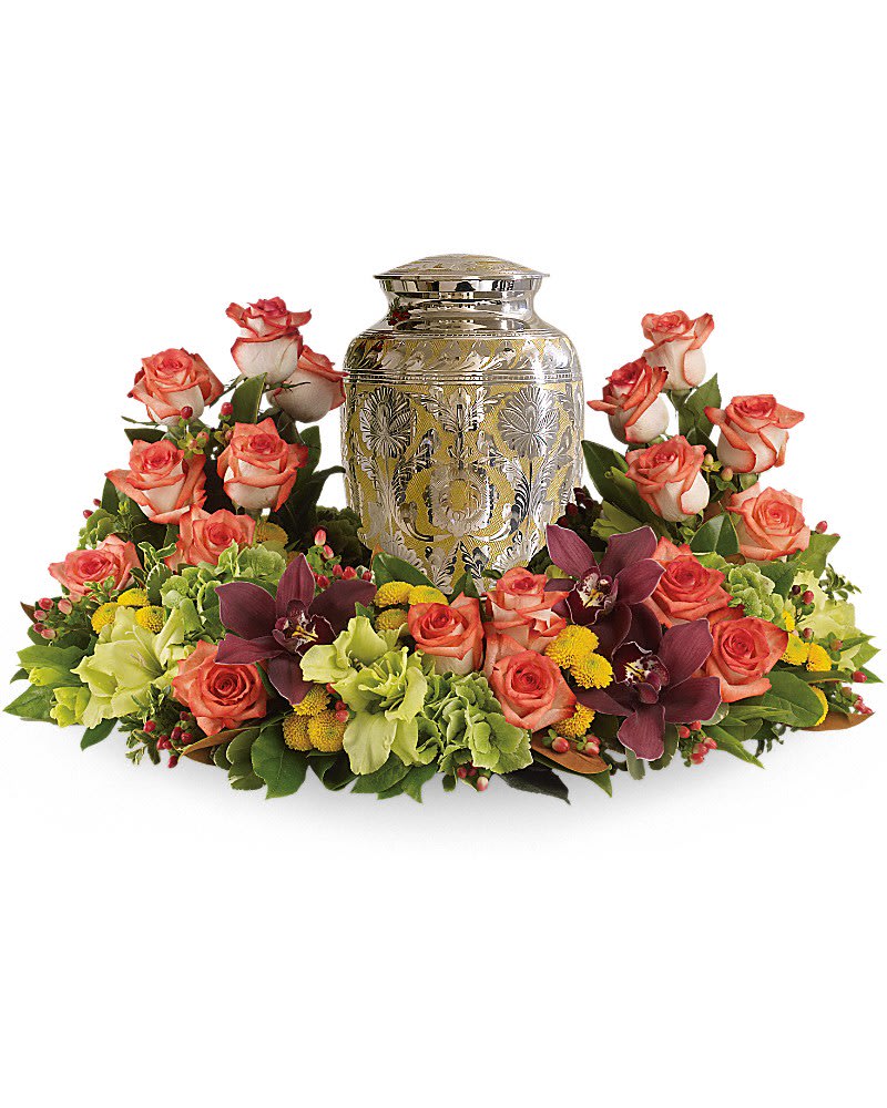 Cremation urn surrounded by a circular arrangement of peach roses, green blooms, yellow accents, and burgundy orchids.