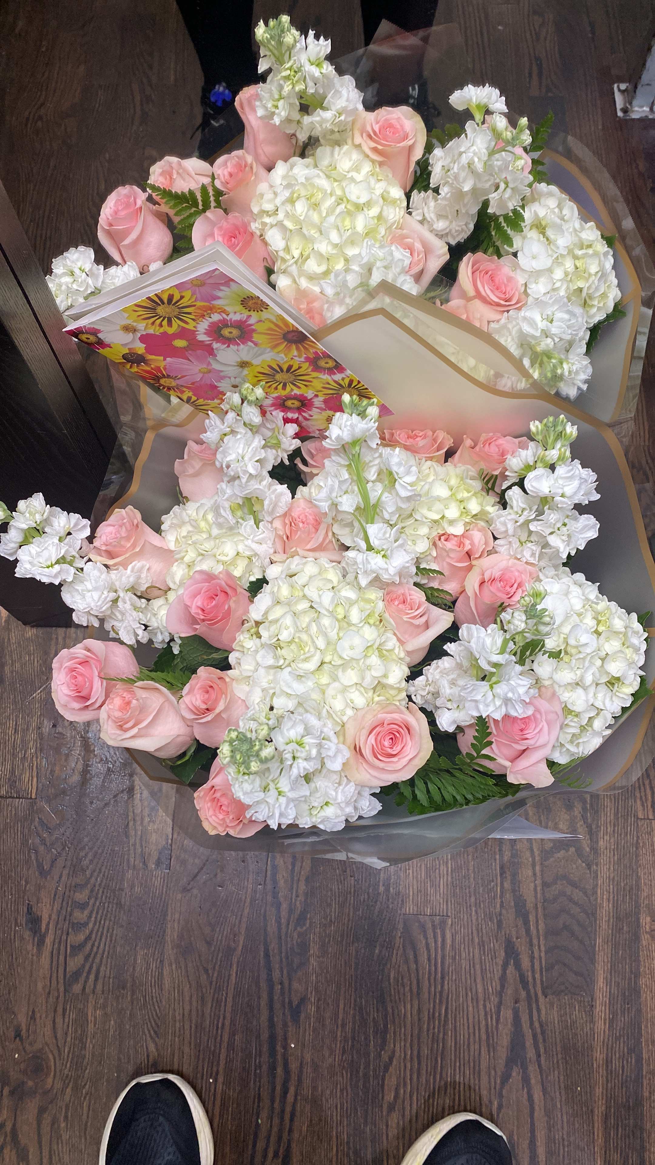 Two bouquets of pink roses and white flowers wrapped in clear paper