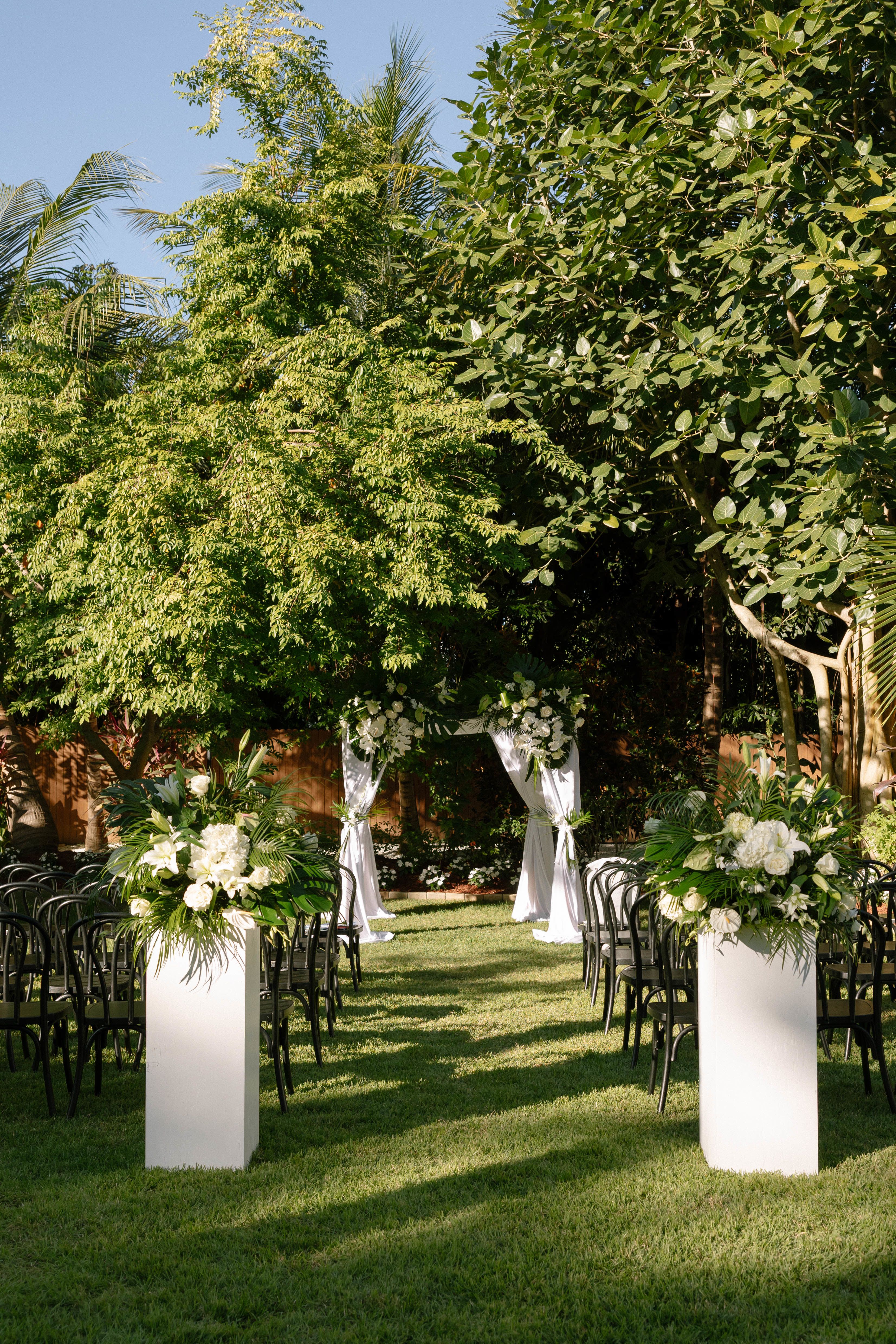 Outdoor wedding aisle with white floral arrangements and a draped arch