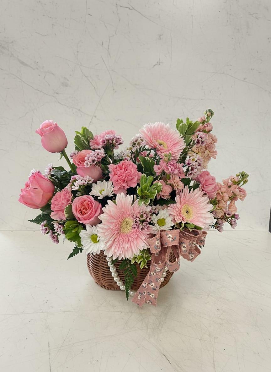 Blooming Garden Basket -  A soft and romantic wicker basket arrangement featuring premium pink expression roses, peach stock, pink carnations, white pom daisies, gerbera daisies, and fresh greenery. Designed with a delicate blend of blush and peach tones, this piece offers a full, airy look that feels both elegant and natural, perfect for gifting or brightening any space.
