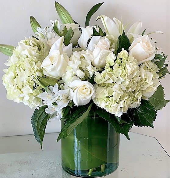 White roses, lilies, and hydrangeas arranged in a clear glass cylinder vase