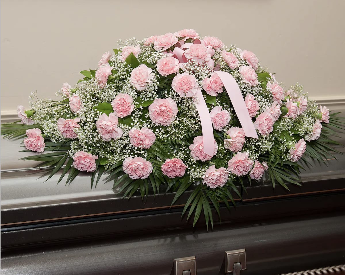 Pink carnation casket spray with baby’s breath and ribbon