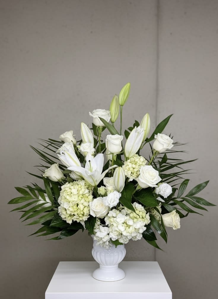 Large white arrangement of roses, lilies, hydrangeas, and carnations in a white pedestal vase