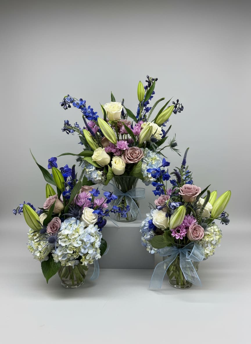 Three pastel floral arrangements in glass vases with blue ribbon bows