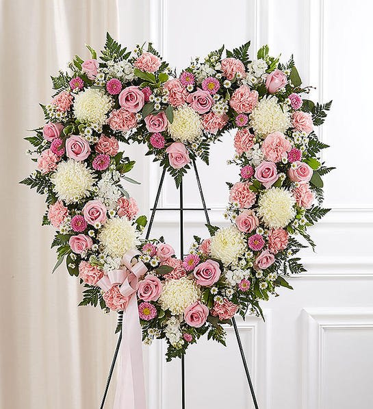 Heart-shaped floral wreath with pink roses and white blooms on a stand