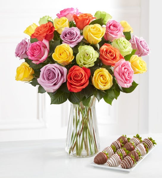 Bouquet of multicolored roses in a clear glass vase with chocolate-covered strawberries