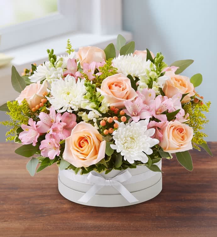 Peach roses and pink flowers arranged in a white round box