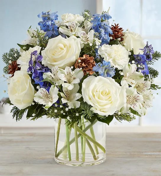 White roses and blue flowers arranged in a clear glass vase