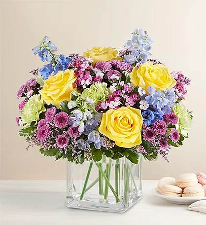 Yellow roses and pastel mixed flowers in a clear square vase