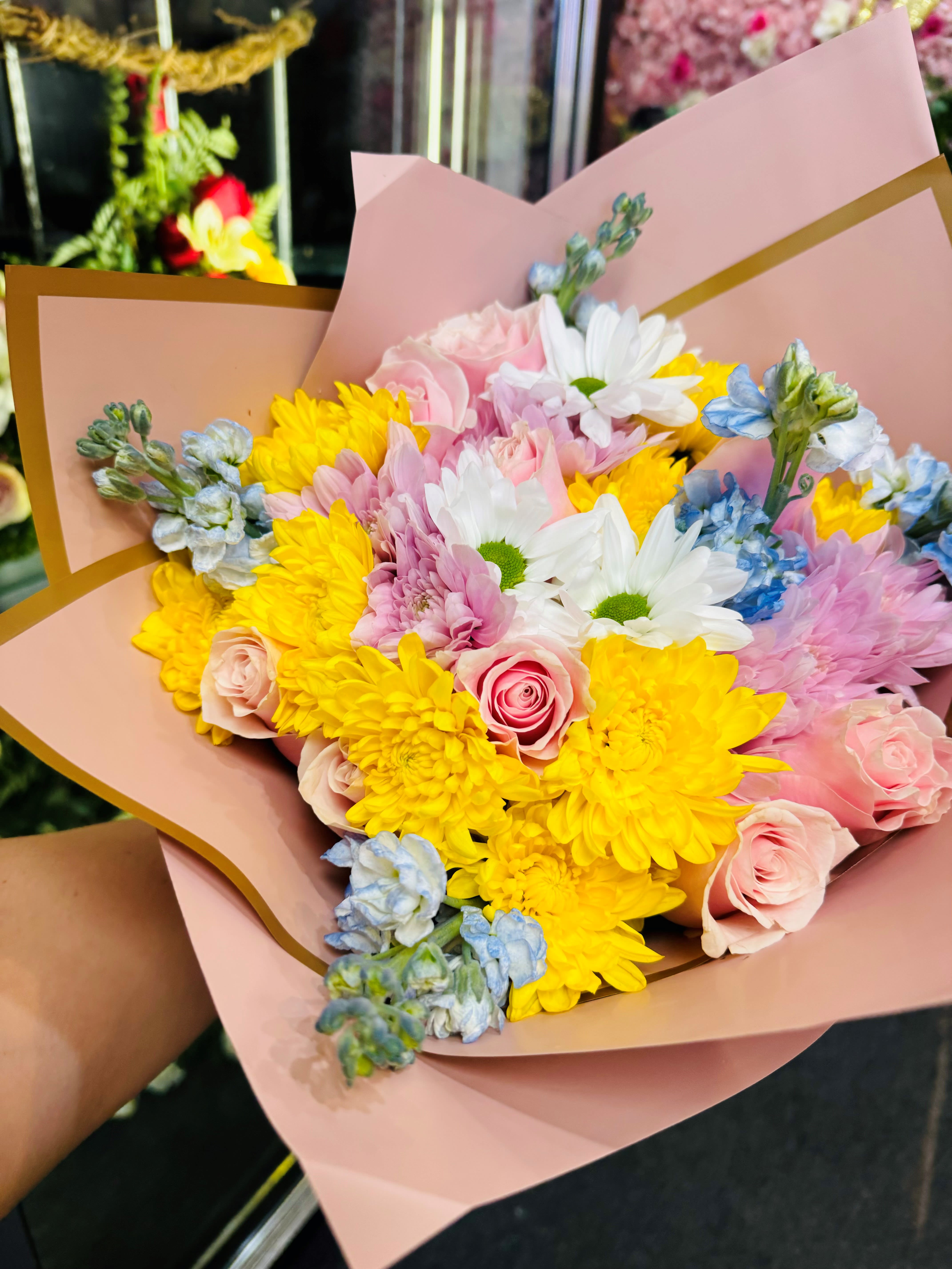 Bouquet of pink roses, yellow chrysanthemums, and white daisies in pink wrap