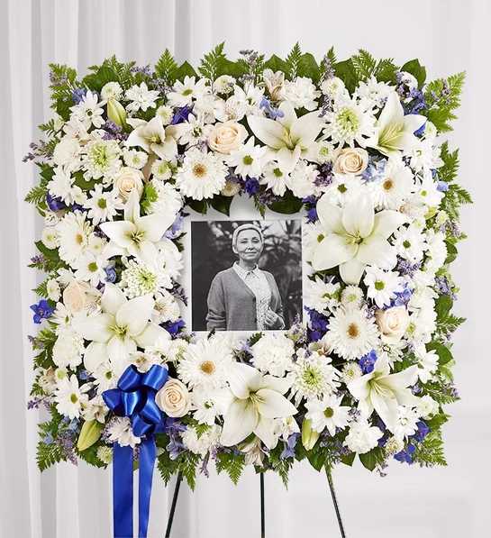 White floral funeral wreath with a photo in the center and blue ribbon