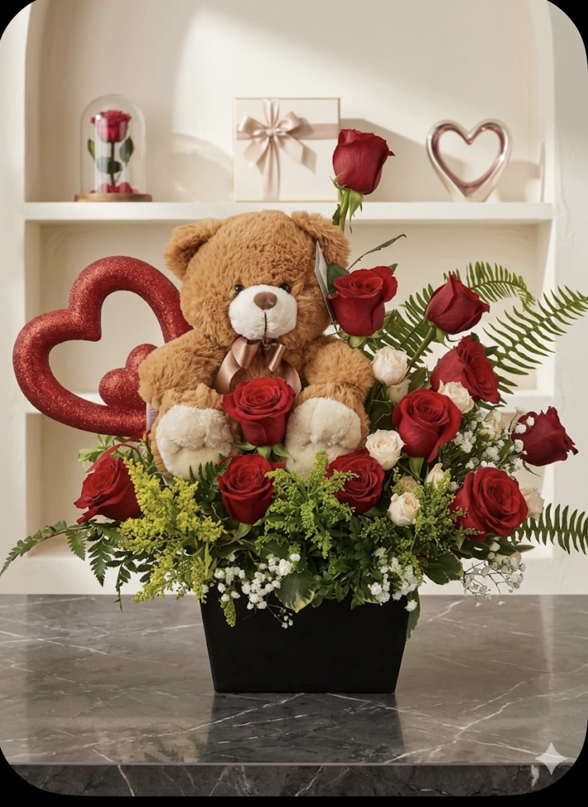 BEAR BOUQUETE - A plush teddy bear peeking out from a sea of red roses creates an instantly romantic birthday bouquet or Valentine's Day arrangement that makes the person you care about feel cherished. This flower arrangement places the bear front and center among densely layered red roses, accented with small white filler blooms, soft green foliage, and a glittery heart for a playful, affectionate finish - perfect for anniversaries, romantic surprises, or saying "I love you."  Thoughtfully presented in a black container with a ribboned gift box and a tiny dome-protected rose included, the set reads as a complete keepsake gift rather than just a bouquet. The mix of velvety red roses, touches of pink and white, and airy greenery gives visual depth and a lush texture; the bear rises above the flowers so the recipient sees both the plush companion and the blooms at once. Order as a romantic gift-set to ensure same-day delivery options (where available); keep blooms in fresh water and away from direct heat to help the roses stay lively.
