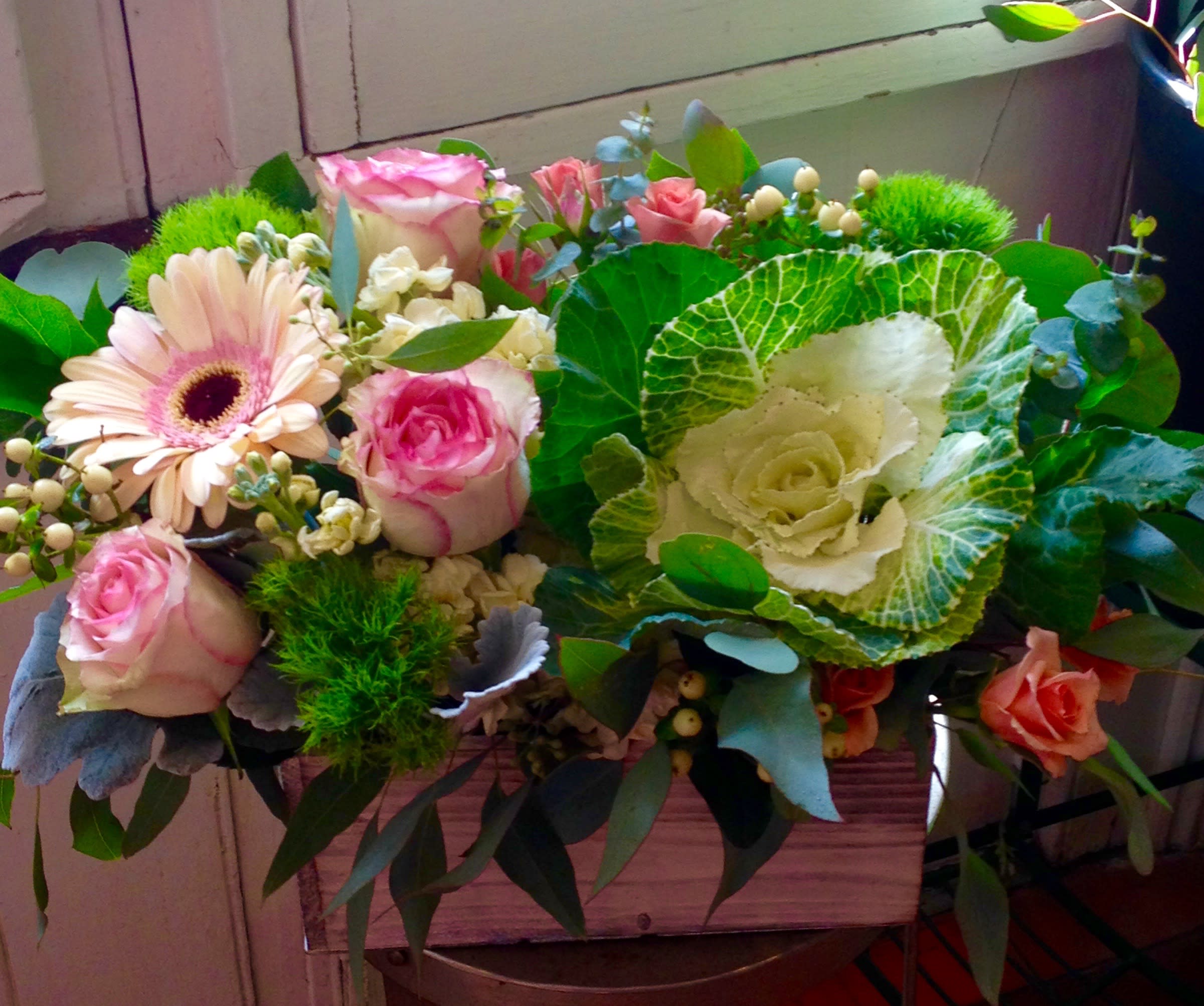 Mixed bouquet of pink roses, a gerbera daisy, and ornamental cabbage in a wooden box