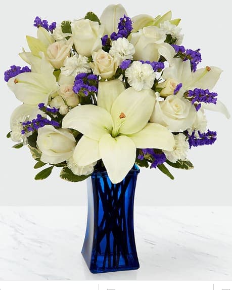 White lilies and roses with purple filler in a blue vase
