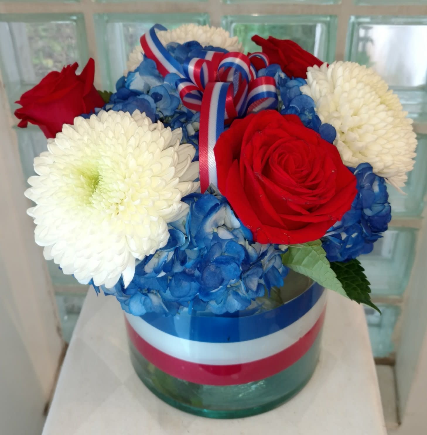 Red roses and white mums arranged with blue hydrangeas in a glass vase.