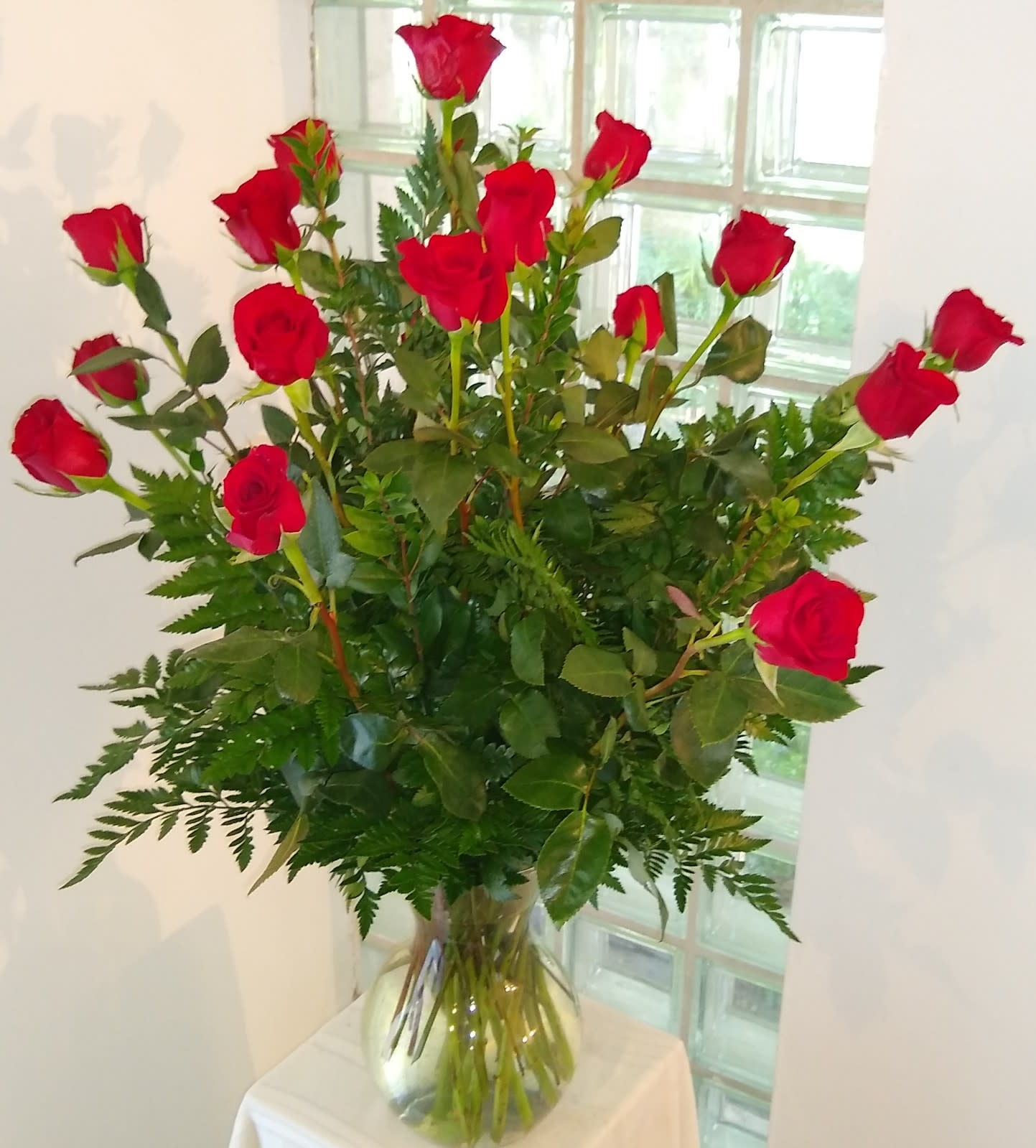 Red roses in a clear glass vase with fern foliage