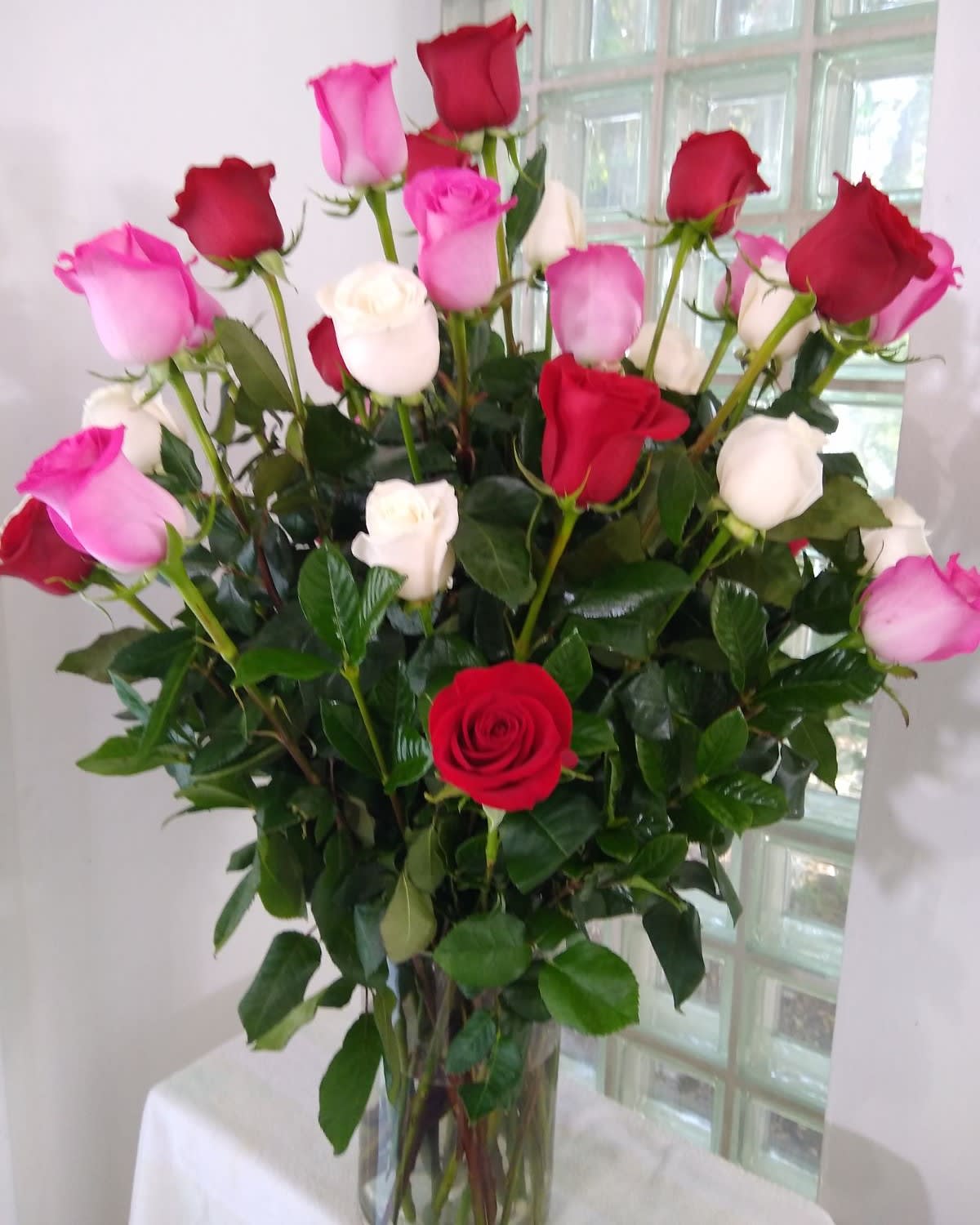 Tall arrangement of red, pink, and white roses in a clear glass vase