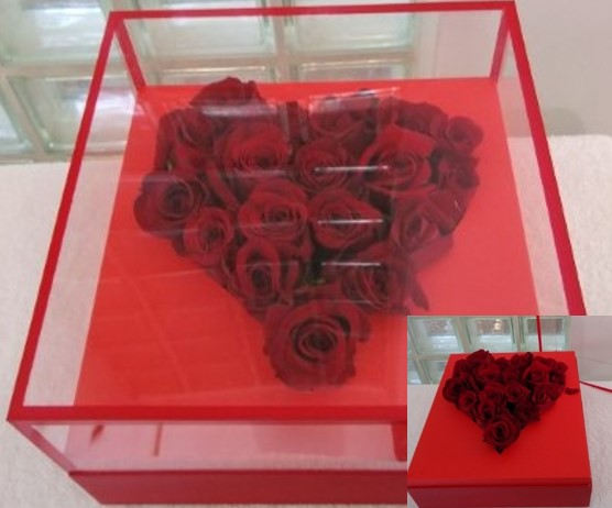 Heart-shaped arrangement of red roses in a clear box with a red base