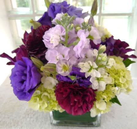 Purple, white, and green floral arrangement in a square glass vase