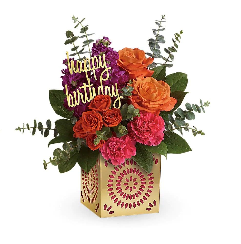 Bright orange roses, pink carnations, and purple blooms in a gold cube vase with a happy birthday pick