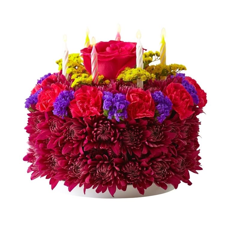 Round floral cake of red and purple blooms topped with a rose and birthday candles