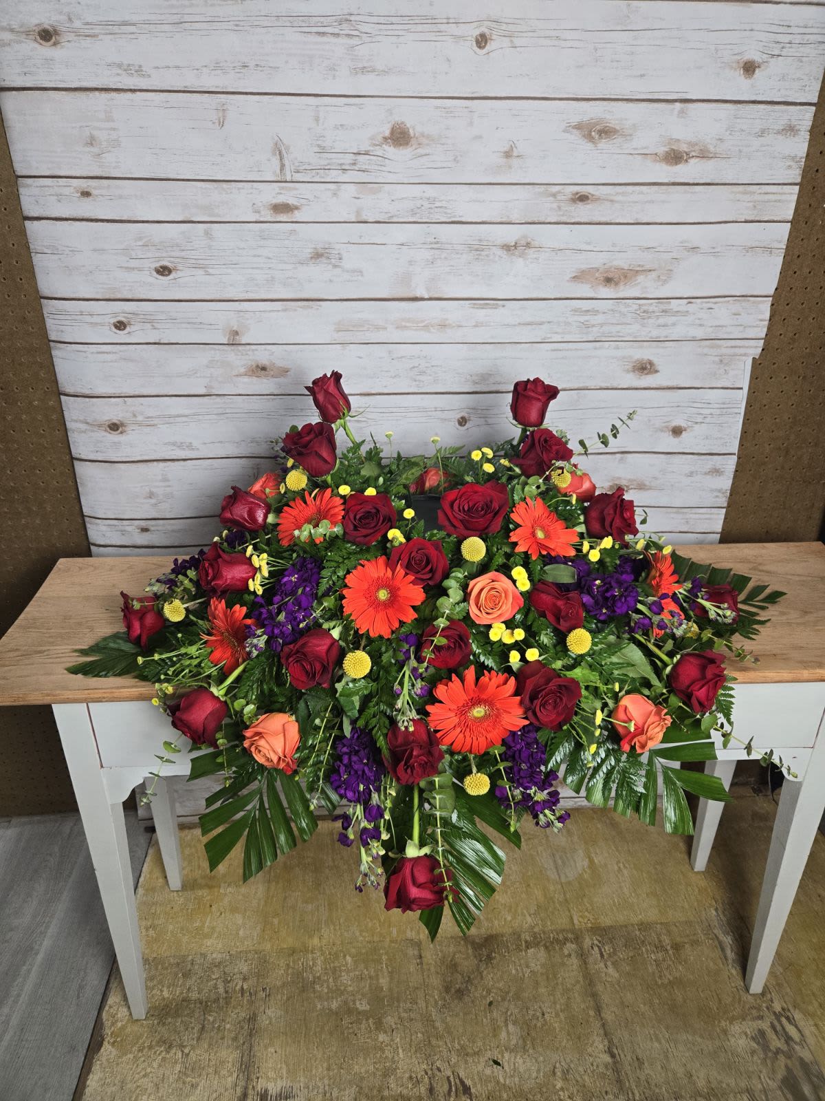 Large arrangement of red roses, orange gerberas, and purple flowers on a table