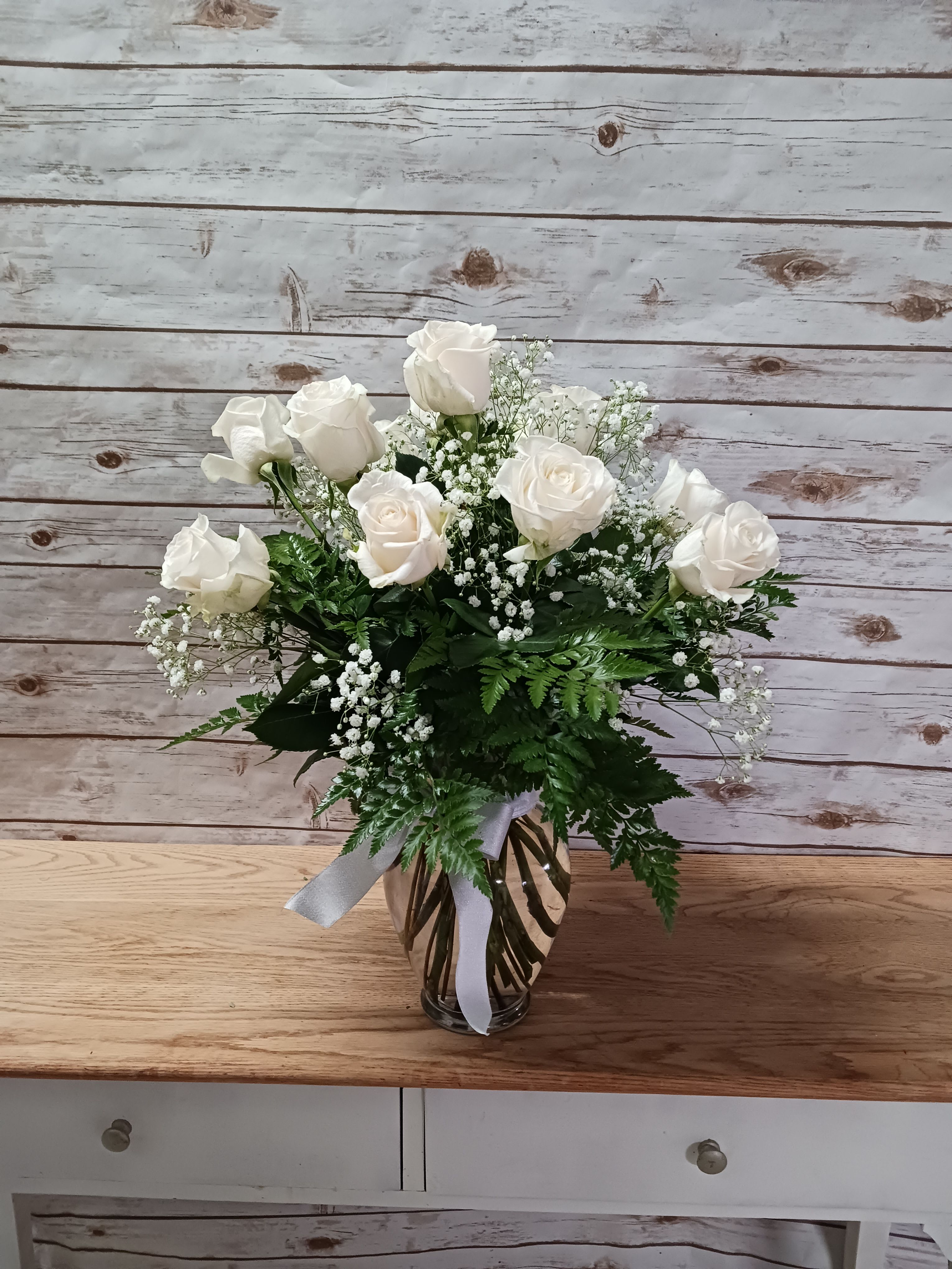 White roses arranged in a glass vase with baby's breath.