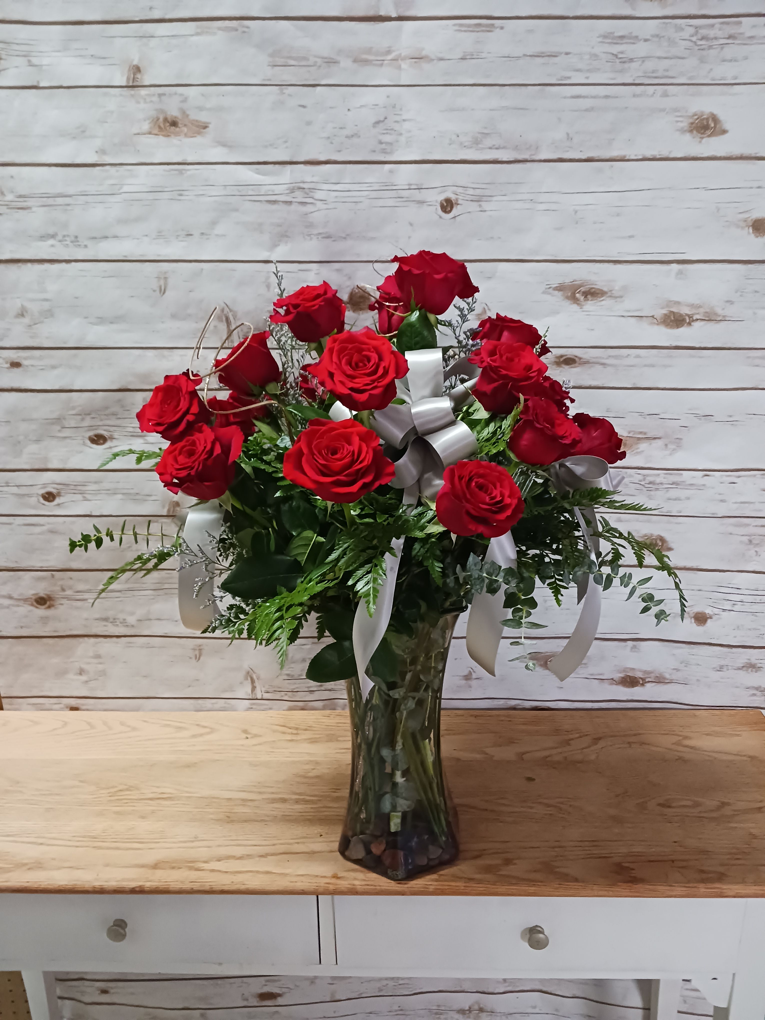 Red roses arranged in a clear glass vase with white ribbons
